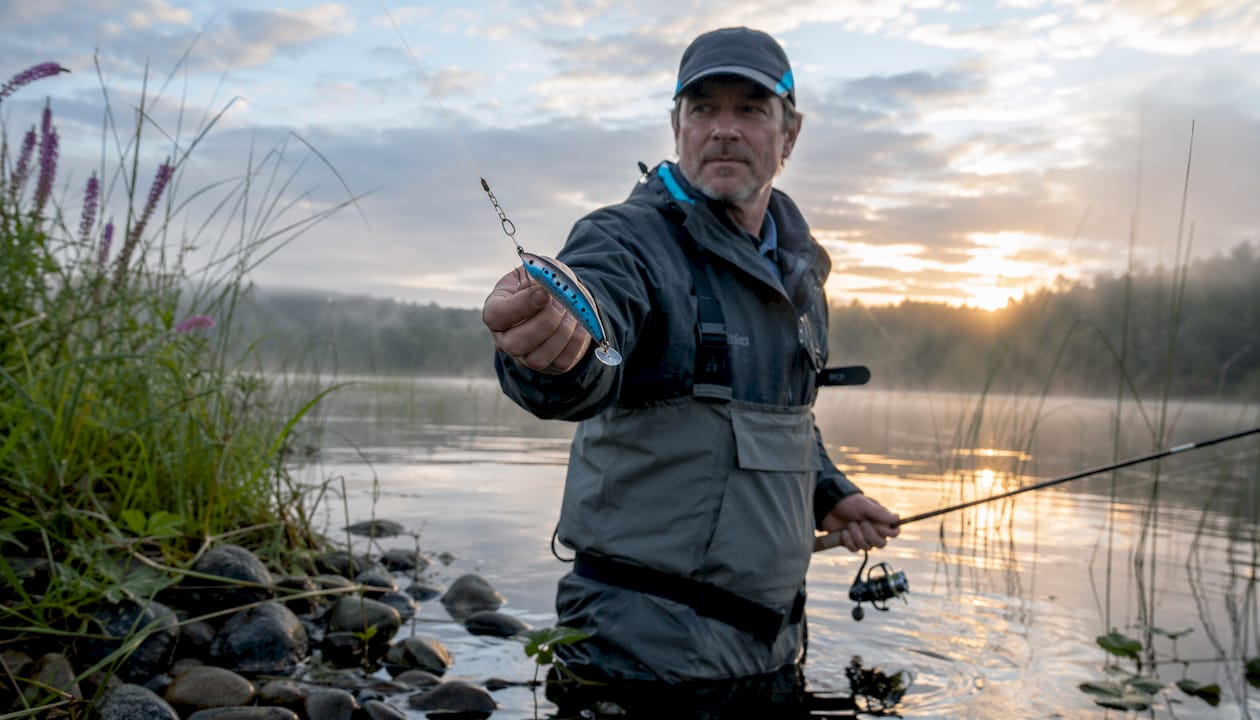 Angler holding Kwikfish lure in river at dawn