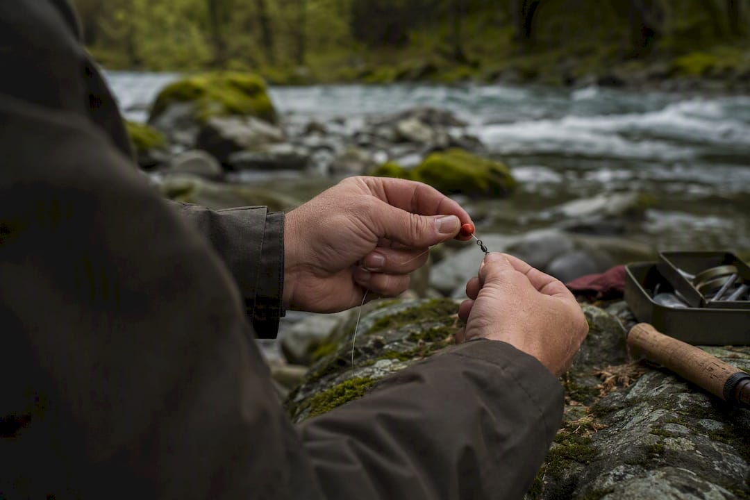 Hands tying sliding sinker rig on riverbank